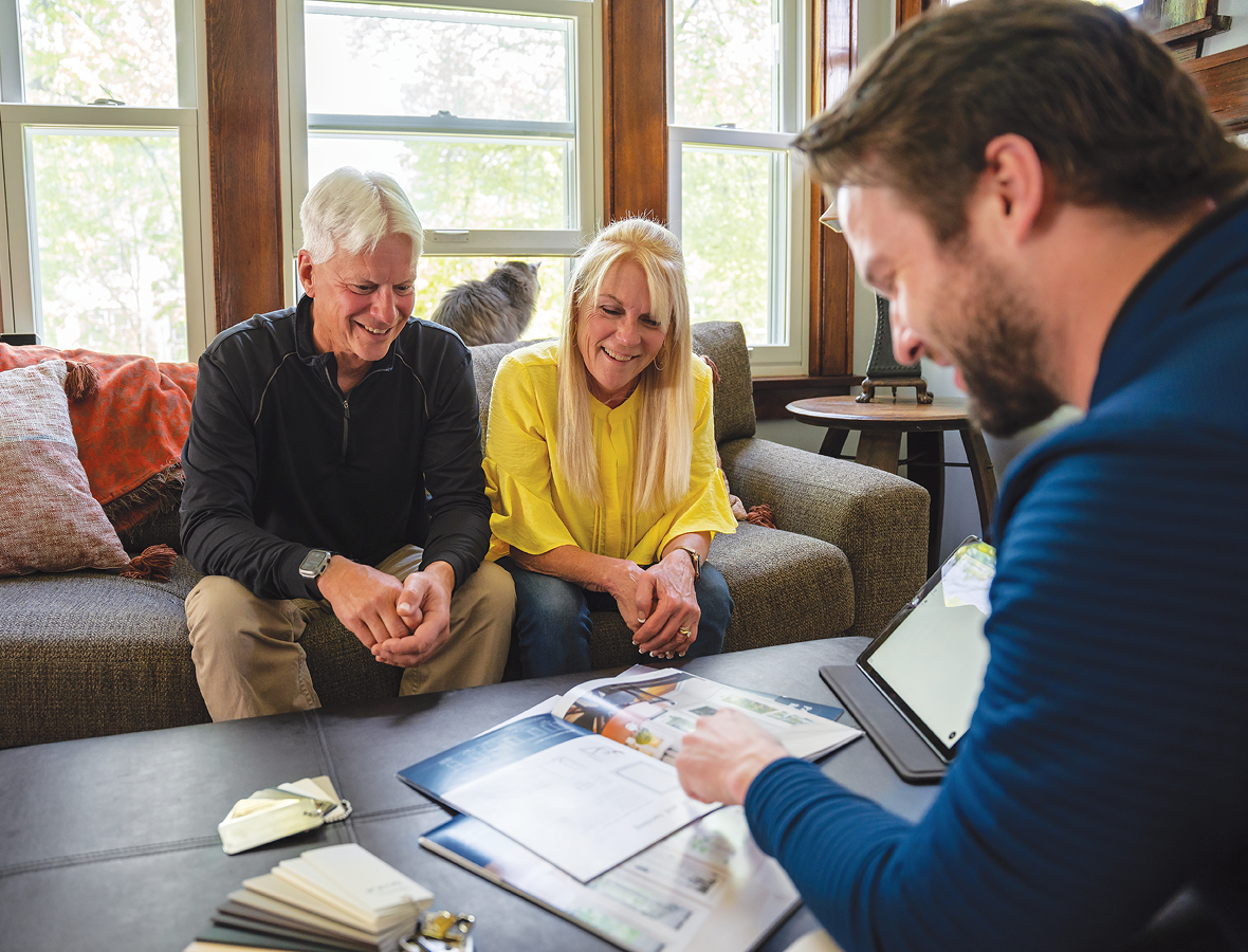 happy couple sitting in living room over looking plans for new windows with Signature Window and Door Employee